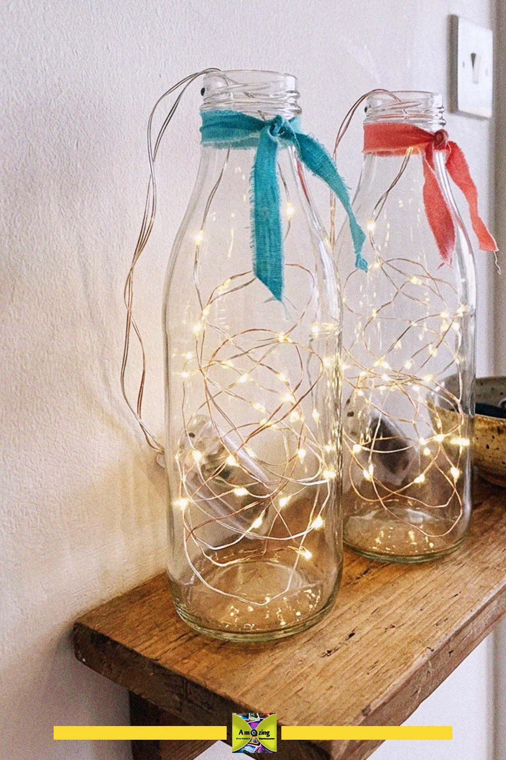 Glass bottle crafts for shelves: two clear bottles filled with warm white fairy lights, tied with blue and red ribbons