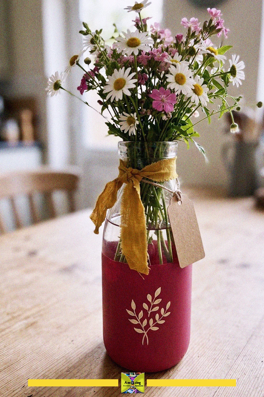 Old glass milk bottle painted pink with a leaf motif, tied with a yellow ribbon and filled with wildflowers as a gift