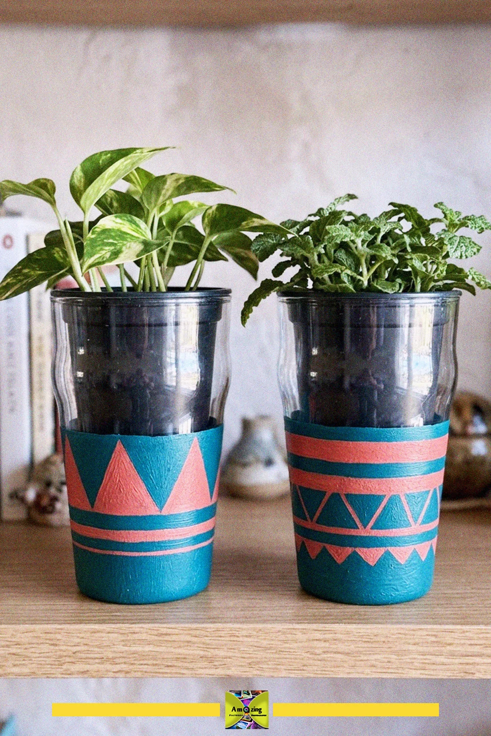 Two upcycled glass cups painted with teal and coral geometric patterns used as covers for small houseplants