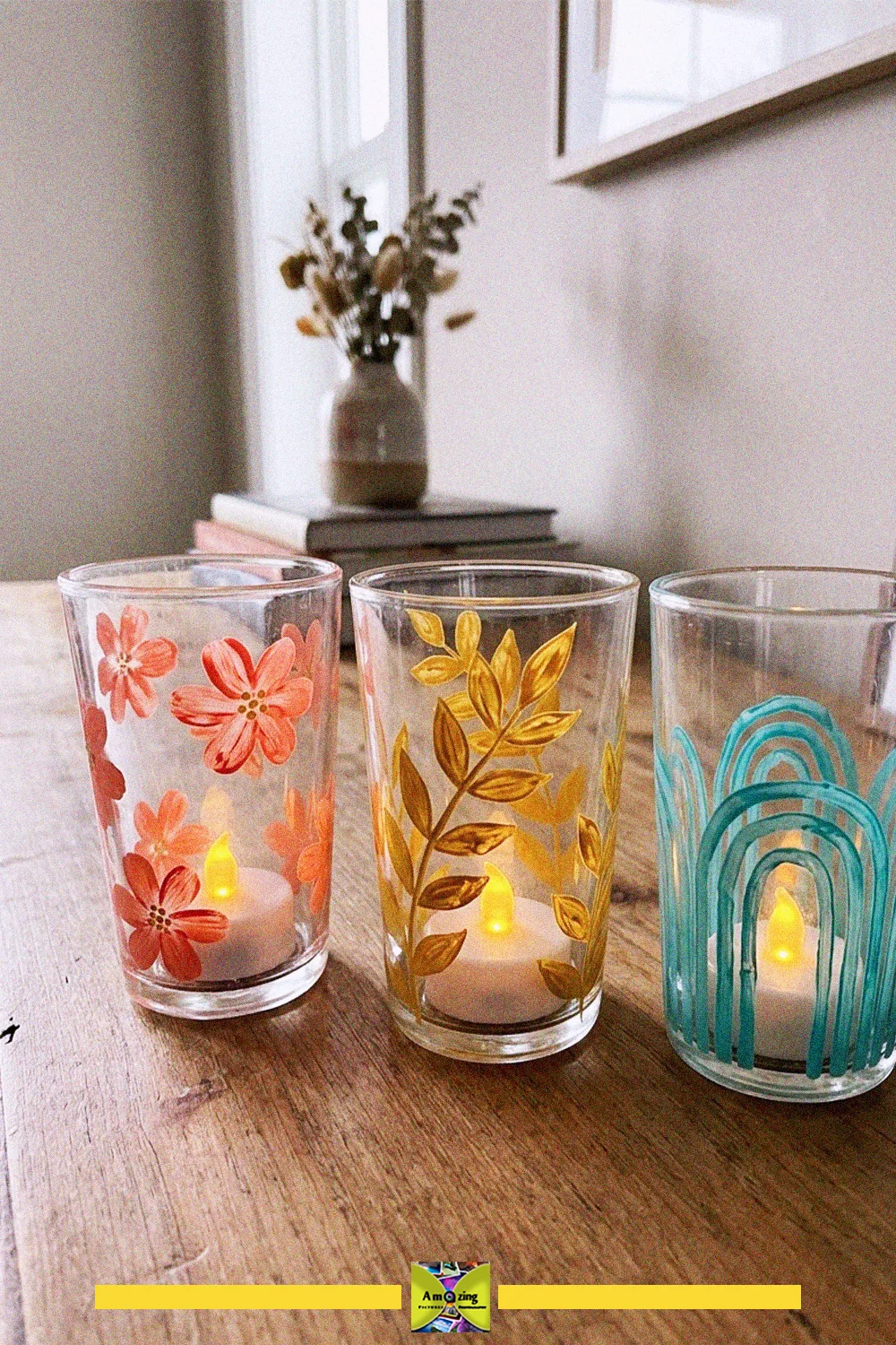 Three old glass cups painted with leaf, floral and geometric designs, glowing with LED tea lights on a wooden table
