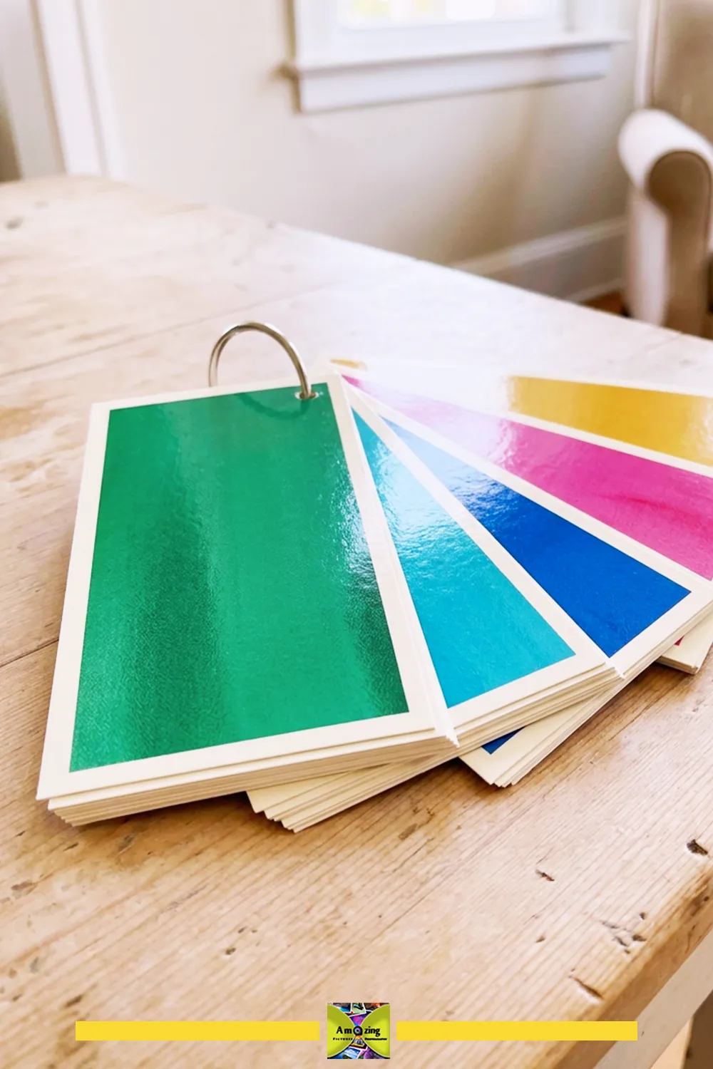 Colorful swatch cards on a metal ring displayed on a wooden table in a bright room.