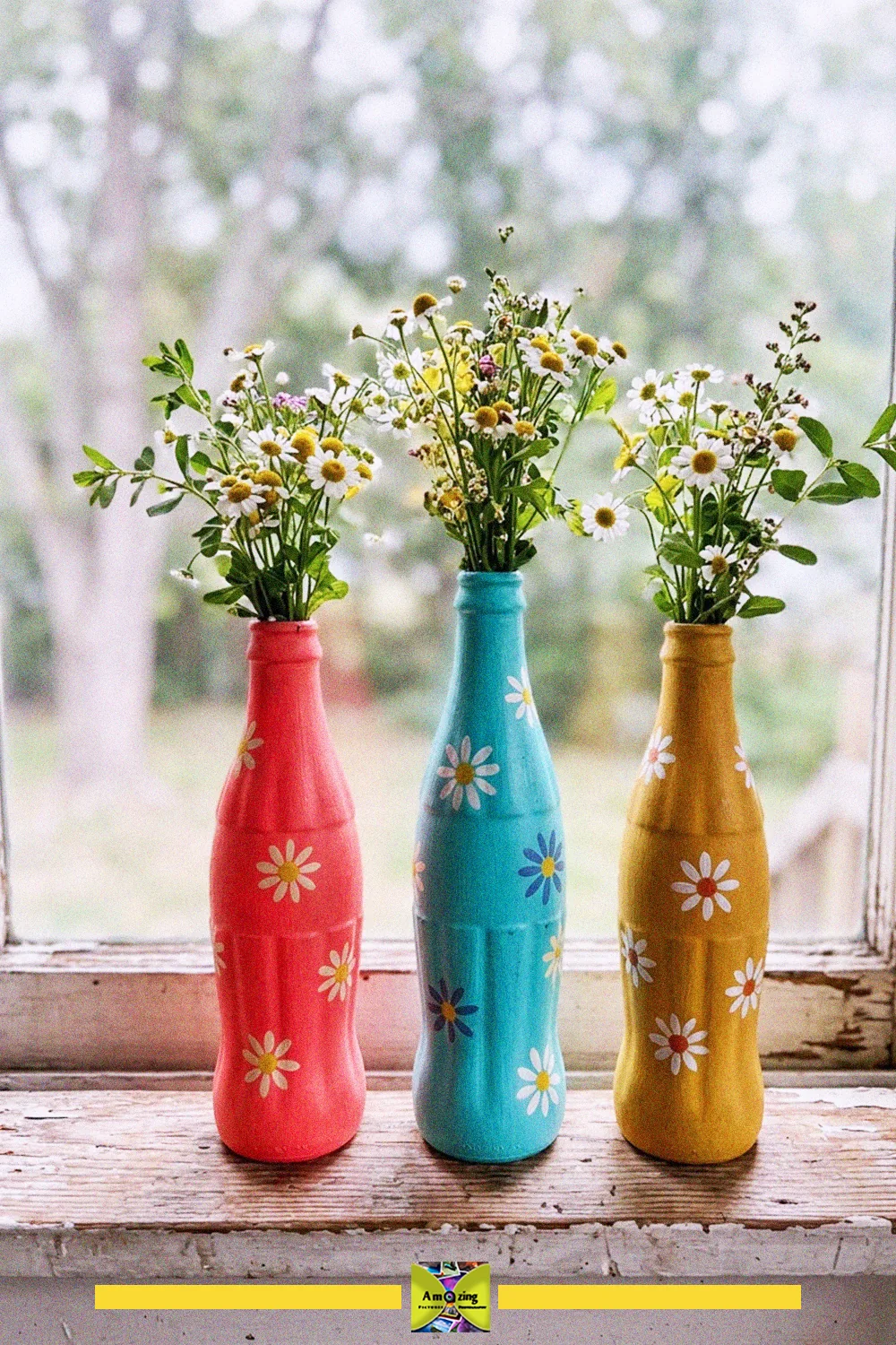 Glass bottle crafts: three old bottles painted pink, blue and yellow with daisies, used as wildflower vases on a windowsill