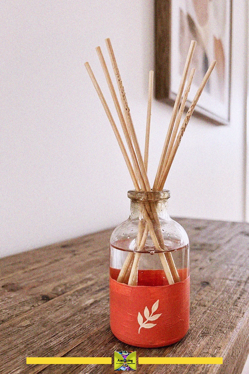 DIY reed diffuser in a recycled glass bottle with an orange paper wrap and leaf design, holding natural reeds