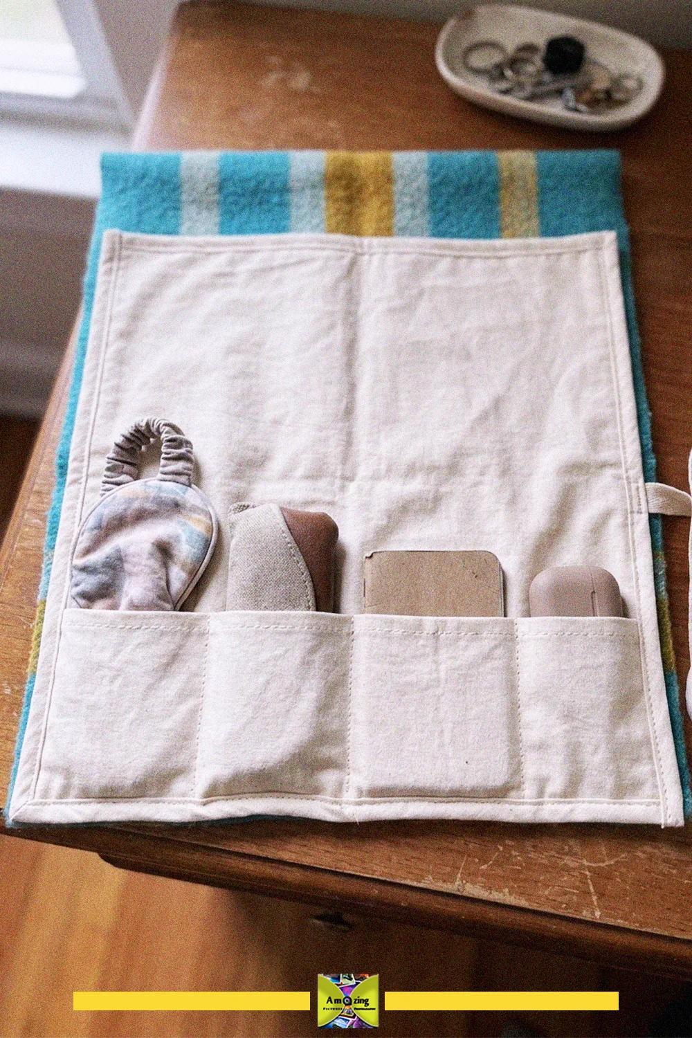 Roll-up travel organizer with canvas pockets and a striped blanket border holding small items