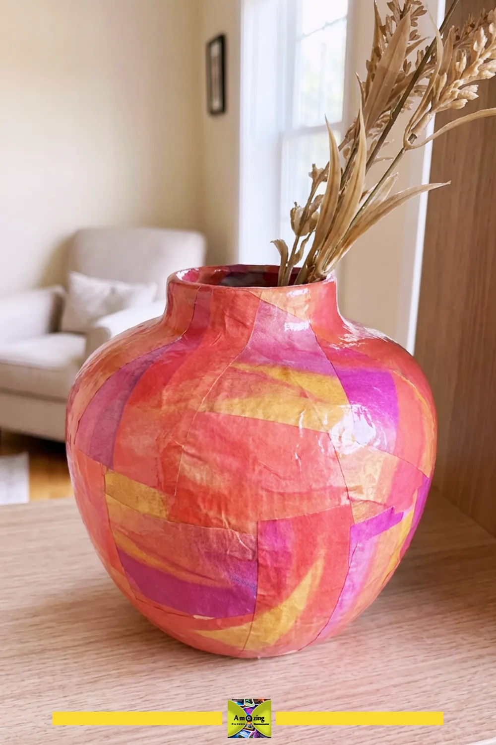 Colorful papier-mâché vase with dried grasses on a wooden table in a cozy living room
